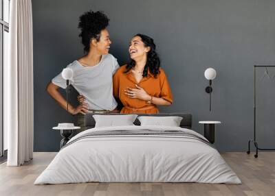 Two women friends embracing and laughing on grey background Wall mural