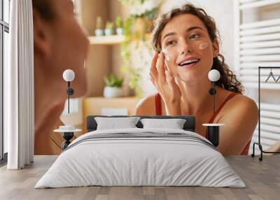 Woman applying moisturiser on face during morning routine Wall mural