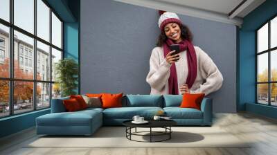 Young black woman in winter clothes using smartphone Wall mural