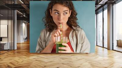 Young woman drinking detox juice with straw on blue wall Wall mural