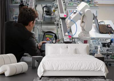 Man is holding teach panel to control a robotic arm which is integrated on smart factory production line. industry 4.0 automation line which is equipped with sensors and robotic arm. Selective Focus. Wall mural