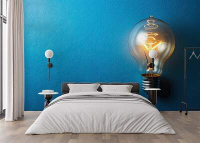 A solitary lightbulb illuminating a blue background with copy space Wall mural