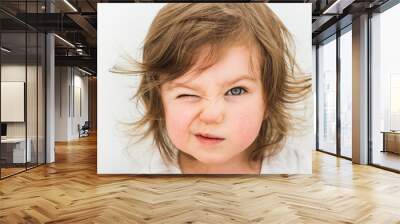 Happy funny baby eyewink isolated on white background. Beautiful close portrait of a girl winking with blue eyes Wall mural