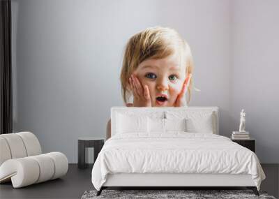 Surprised shocked child toddler girl with hands on her cheeks isolated on light background Wall mural