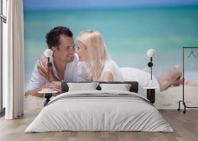 Cheerful couple embracing and lying on the beach on a sunny day Wall mural