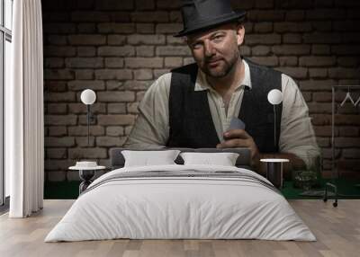 Poker player sitting behind the poker table with cards and playing chips  -  poker in a dark back room with a brick wall Wall mural