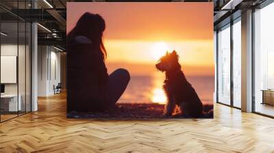 Woman and terrier dog sitting on rocky beach watching sunrise. Wall mural