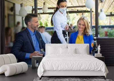 Handsome couple having lunch in the restaurant, being served by waitress with a mask, corona time Wall mural