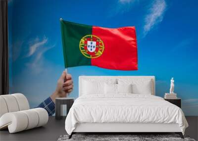 Hand holding Portugal national flag on blue sky. Wall mural