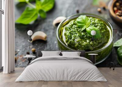 Glass bowl of homemade fresh basil pesto placed on a rustic kitchen surface with herbs and spices. Wall mural