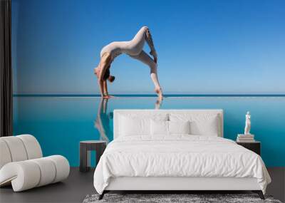 Beautiful athletic slim woman doing One legged Wheel exercise, Bridge pose standing on the edge of a blue water pool against the sky while relaxing at a spa resort. Copyspace Wall mural