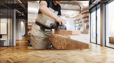 Carpenter working with electric planer on wooden plank in workshop. Craftsman makes own successful small business. Wall mural