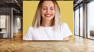 Close-up portrait of a positive smiling young blond woman with close eyes on a yellow background. Place for advertising Wall mural