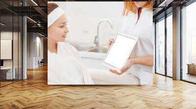 Cosmetologist shows her patient a woman an ultrasonic facial cleaning procedure on tablet. Concept of rejuvenation and cleansing. White screen, mockup Wall mural