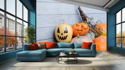 Pumpkins and jack lantern of different colors and sizes lie on gray wooden wall background with jug and pumpkins hanging on it. Concept of Halloween celebration and joy of harvest period. Copyspace Wall mural