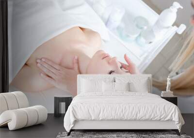 Young woman beautician doing neck and face massage to beautiful and charming young caucasian female client lying on couch under white blanket. Concept of cosmetic procedures and anti-aging products Wall mural