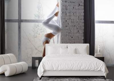 Young woman dressed in white sportswear practicing yoga in a urban background. Yogi handstand in pose shirshasana or Sirshasana near a picture window with white brick wall. horizontal shot Wall mural