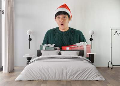 Excited young asian man wearing santa clause hat and green long sleeved sweater is carrying large gift box with ribbon, isolated over white background. Concept for Christmas Holiday and New Year Party Wall mural