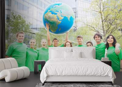 Portrait of team in green t-shirts lifting globe overhead Wall mural