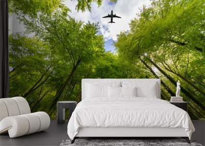 Airplane flying over a lush green woodland, looking up. Wall mural