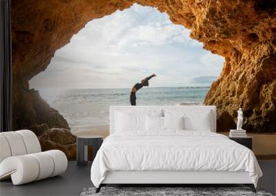 Fit, sporty woman doing a backbend exercise by the sea in a cave Wall mural