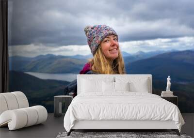 Woman smiling and happy while hiking Ben Nevis mountain, Scotland, UK with a winter hat and a beautiful backdrop of mountains and lakes Wall mural