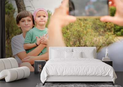 Child with pink headscarf taking a photo with his brother Wall mural