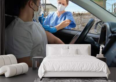 Nurse performing vaccination on young man in car Wall mural