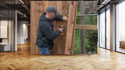 A white, middle-aged gay man builds a wooden fence in his back yard. Wall mural