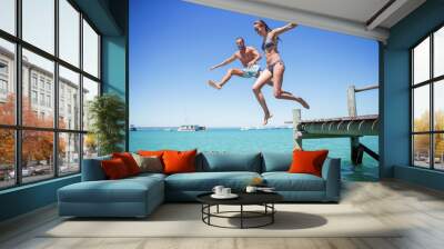 Couple jumping off wooden dock into water Wall mural