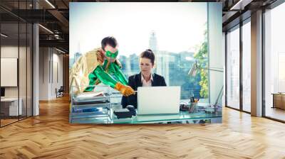 Superhero helping businesswoman working at office desk Wall mural