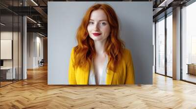 Confident young British entrepreneur with red hair wearing a stylish yellow blazer, smiling while looking at the camera in a bright portrait setting Wall mural