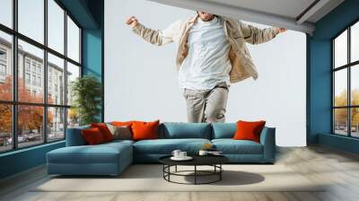 Excited young man jumping in casual attire against a white background Wall mural