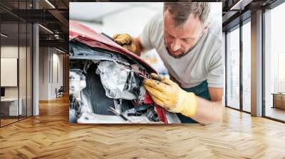 Experienced repair worker fixing front of a damaged car at an auto repair shop with focused attention and precision Wall mural