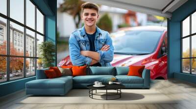 Happy teenage male standing beside a new red car smiling confidently in a suburban neighborhood Wall mural