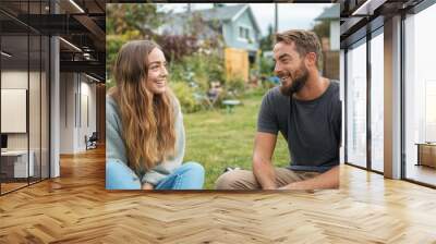 Happy young woman talking with male friend outdoors in a garden setting, sharing cheerful conversation with nature and homes in the background, showcasing a moment of friendship and relaxation. Wall mural