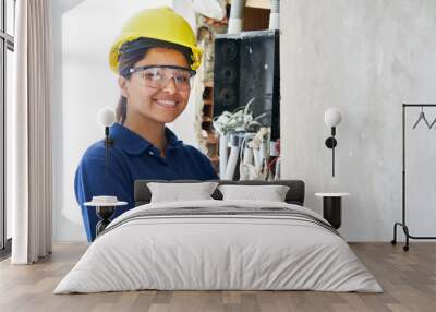 Portrait of smiling young female electrician using pliers while fixing wires in wall at incomplete house construction site Wall mural