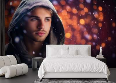 Portrait of a handsome young man in a hood on a snowy background. Wall mural