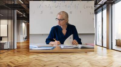 Portrait of high school math teacher sitting at desk working on assignments for students. Wall mural