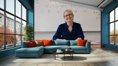 Portrait of high school math teacher sitting at desk working on assignments for students. Wall mural