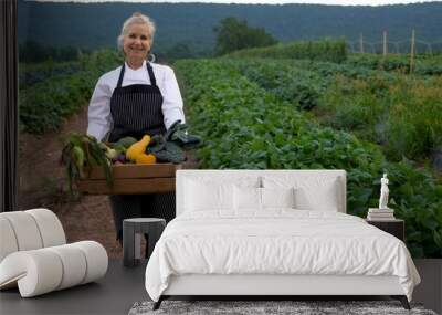 Portrait of pretty, caucasian, female chef carrying fresh picked vegetables walking towards camera on a farm for farm to table at sunrise sunset. Wall mural