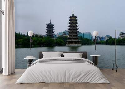 two asian pagodas (Sun Moon Pagoda) above peaceful lake. Reflection in water. Forest trees and city skyline as background. In Guilin city Guangxi China. Wall mural