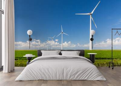 A long row of wind turbines emerging from green grass and against a summer blue sky with distant clouds Wall mural