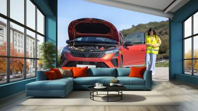 A young pretty female driver puts on the reflective safety vest to check the car that has broken down, broken engine on her trip, roadside assistance, travel insurance Wall mural