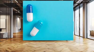 Close-up two white and blue capsules isolated on light blue background, top view, left side, copy space Wall mural