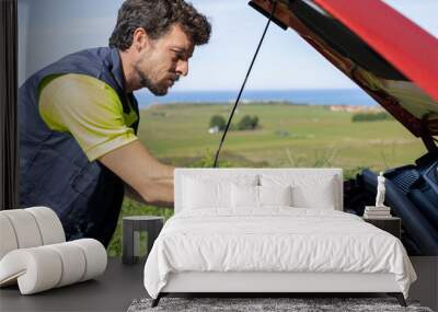 Young professional mechanic man in work uniform repairs a broken down car on the road with the hood raised, checks oil and fluid levels, roadside assistance, insurance tow truck Wall mural