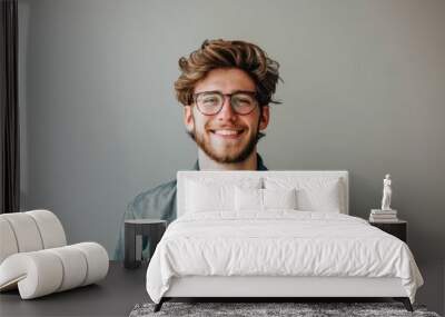 Portrait of a smiling young man with glasses and a denim jacket against a neutral gray background. Wall mural