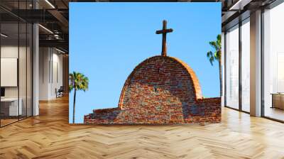 Detail of old cross on top of a curved arch with a palm tree in the background Wall mural