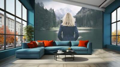 Blonde woman standing backwards and watching magic lake in mountainous country landscape. Wall mural