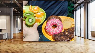 Healthy and unhealthy. Two plates of sweet snacks, Biscuits and fruit, A woman reaching out for healthy food. Wall mural